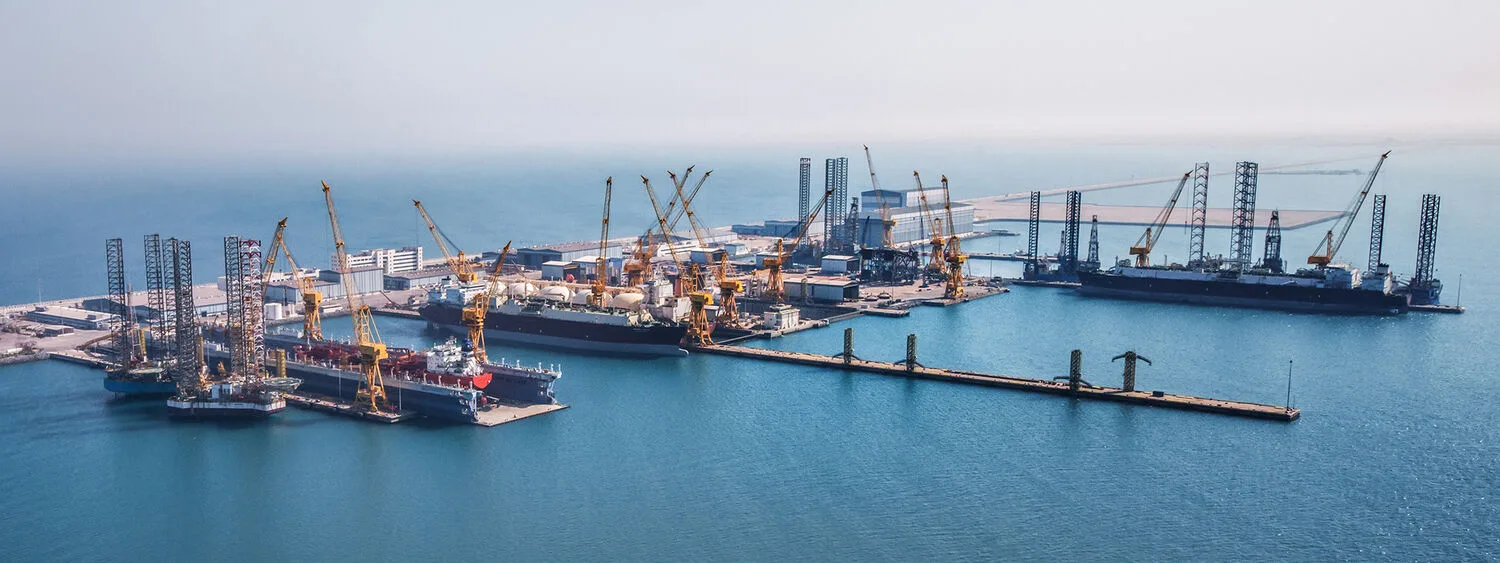 Aerial view of N-KOM shipyard with oil rigs, large vessels, cranes, and industrial buildings surrounded by water