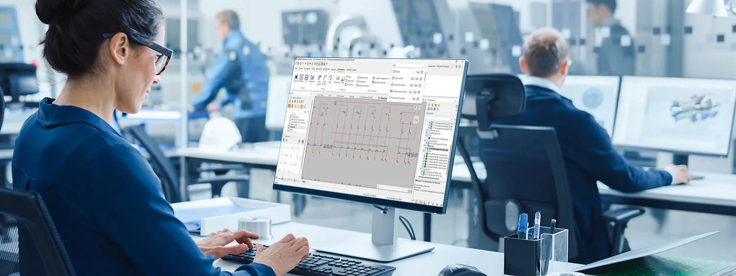 Person working on CADMATIC Electrical software in a modern office, with others at desks using computers for engineering tasks