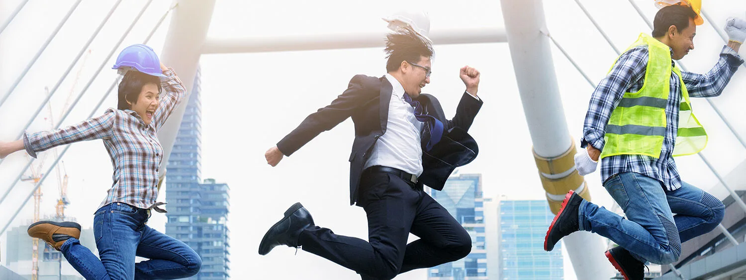 Three people jumping and smiling building and construction site in the background