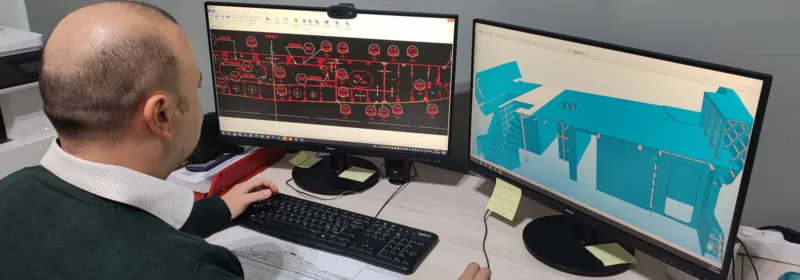 Henkilö työskentelee työpöydän ääressä, jossa on kaksi monitoria, joissa näkyy tekninen piirustus ja 3D-malli, jotka liittyvät superjahdin lohkon suunnitteluun.