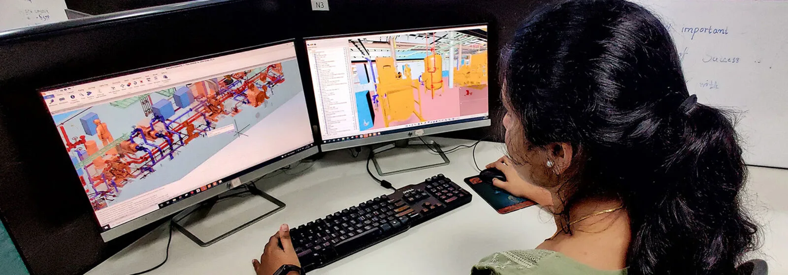 Person working at a desk with two monitors displaying 3D marine CAD models, with a whiteboard in the background