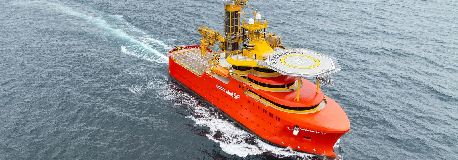 Bright orange offshore support vessel 'Edda Wind' with helipad, navigating the ocean and equipped for offshore wind operations.