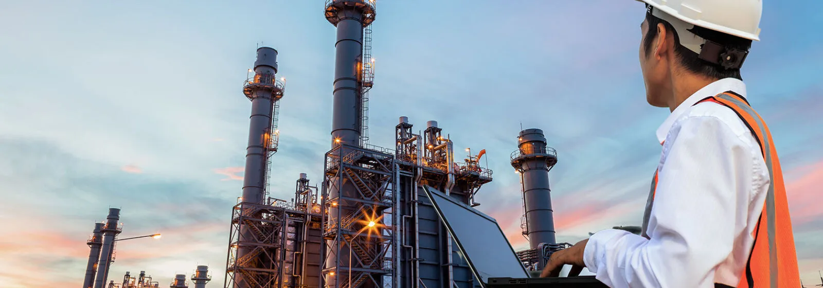 Oil refinery at dawn and engineer working on a computer