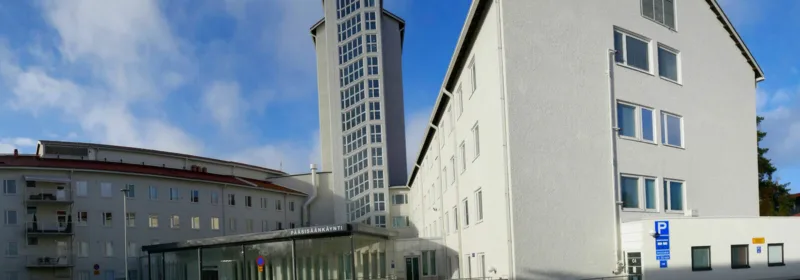 Exterior view of North Karelia Central Hospital with white facade, glass tower, and entrance marked 'PÄÄSISÄÄNKÄYNTI