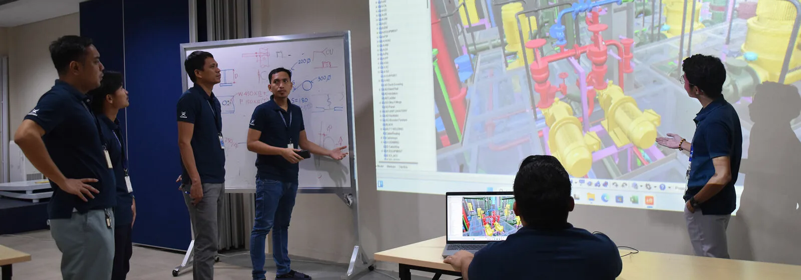 Five people in a meeting room reviewing 3D maritime design models on a laptop and projected screen, with diagrams on a whiteboard