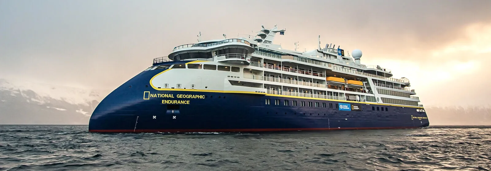 Expedition cruise ship 'National Geographic Endurance' sailing in open waters with snowy mountains in the background