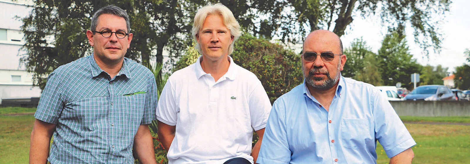Three people seated outdoors with trees and parked cars in the background, faces obscured for privacy