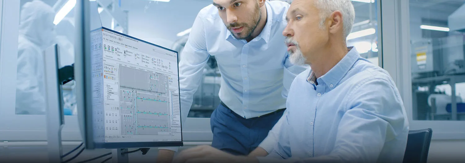 Two professionals reviewing CADMATIC Electrical software interface with charts and data tables in a technical workspace