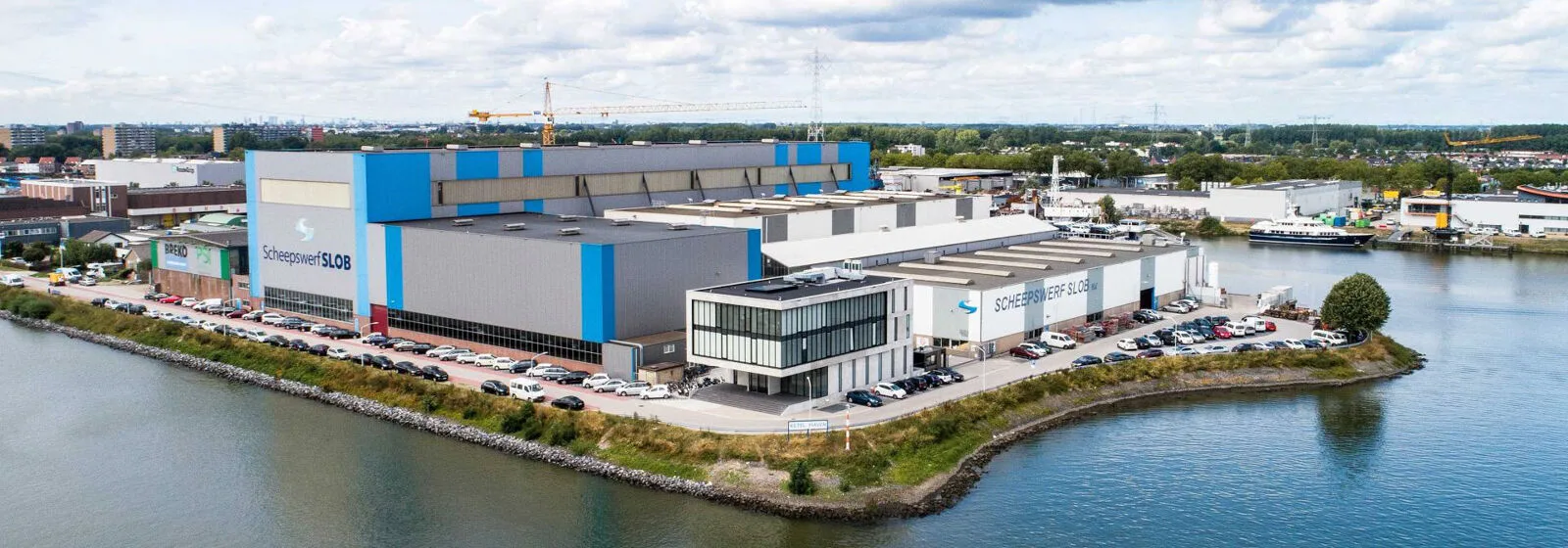 Aerial view of Scheepswerf Slob shipyard with industrial buildings, parked cars, cranes, and surrounding water and greenery