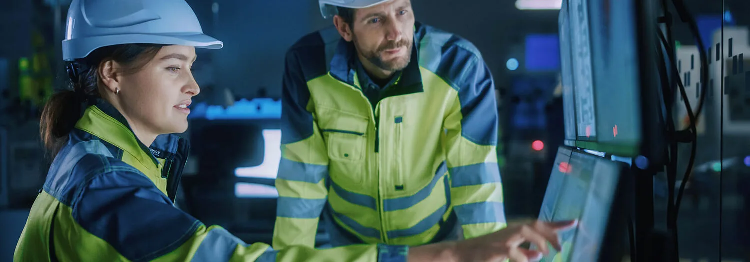 Two engineers in an industrial plant are looking at monitors