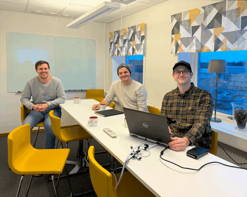 Three engineers in their office space smiling at the camera over Cadmatic software